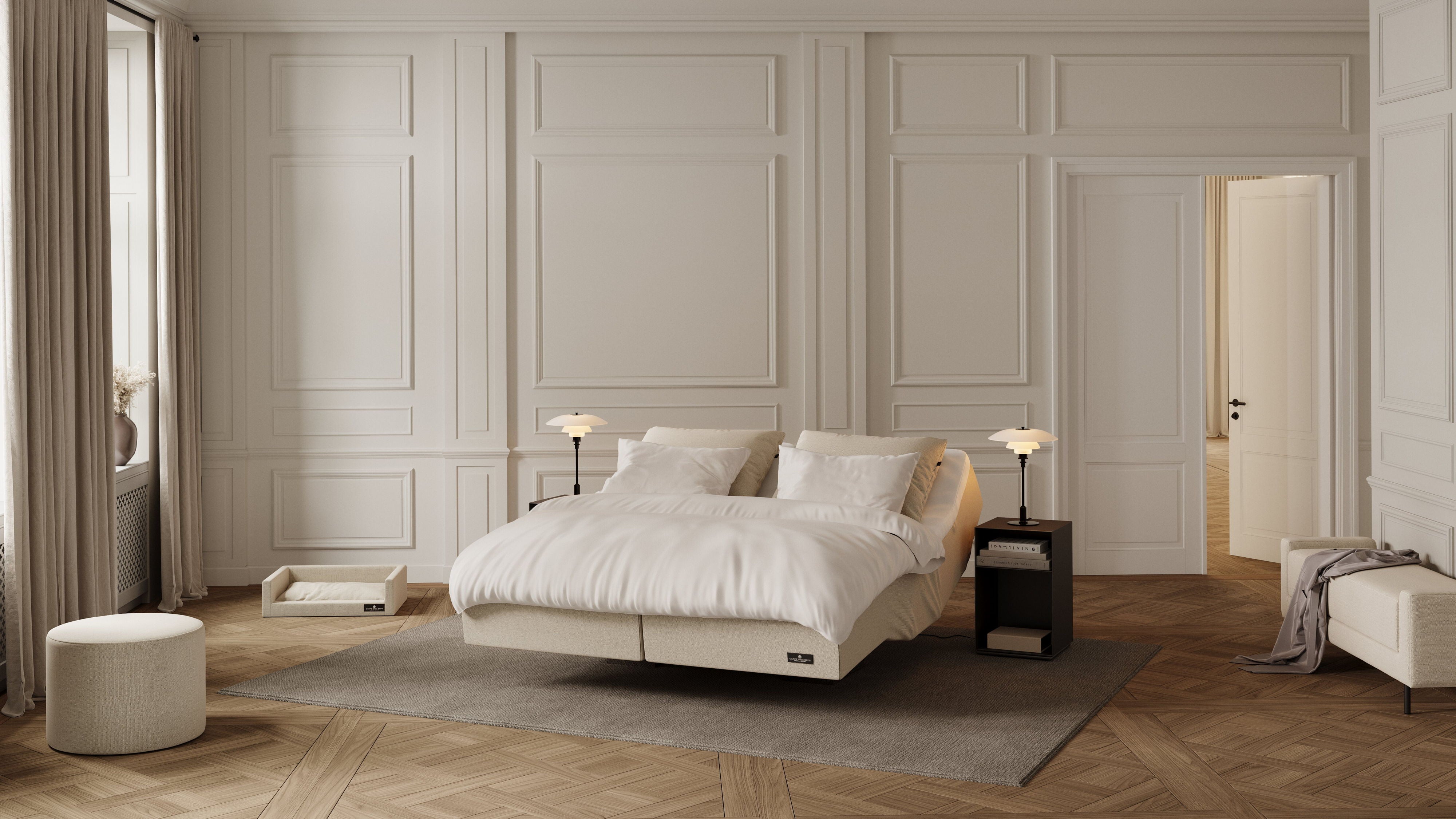 A modern platform bed with white bedding and pillows, styled in a luxurious bedroom with cream paneled walls, a herringbone wood floor, and a gray rug.